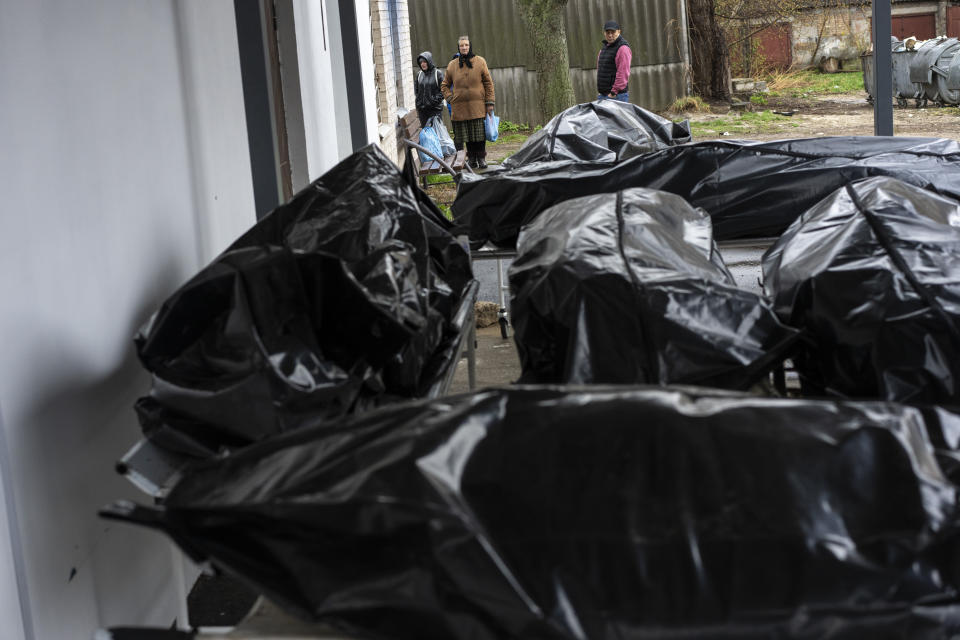 Nadiya Trubchaninova, 70, looks at the black bags containing the bodies of dead civilians, while she waits for her son's body to be delivered to the morgue so that she can have a decent burial in the cemetery of Mykulychi, on the outskirts of Kyiv, Ukraine, Saturday, April 16, 2022. After nine days since the discovery of Vadym's corpse, finally Nadiya could have a proper funeral for him. This is not where Nadiya Trubchaninova thought she would find herself at 70 years of age, hitchhiking daily from her village to the shattered town of Bucha trying to bring her son's body home for burial. (AP Photo/Rodrigo Abd)