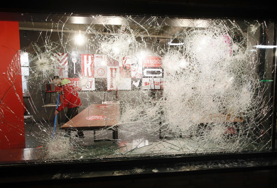 A man cleans up and is seen through the damaged glass in a fast-food restaurant that was smashed in protests against a nation-wide curfew in Rotterdam, Netherlands, Monday, Jan. 25, 2021. The Netherlands Saturday entered its toughest phase of anti-coronavirus restrictions to date, imposing a nationwide night-time curfew from 9 p.m. until 4:30 a.m. in a bid to control the COVID-19 infection rate. (AP Photo/Peter Dejong)
