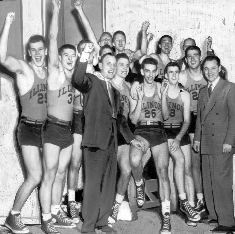 University of Illinois coach Harry Combes, foreground center, raises a fist with his team after beating North Carolina State in an NCAA Tournament college basketball quarterfinal game in New York in 1951. In street clothes are assistant coach Howie Braun, front right, and trainer Ike Hill, obscured at rear right. Players identified are: Bob Peterson (25), Herb Gerecke (38), Irv Bemoras (26), and Ted Beach (8). Illinois advanced to the national semifinals against Kentucky where they lost 76-74. . (Chicago Tribune via AP)