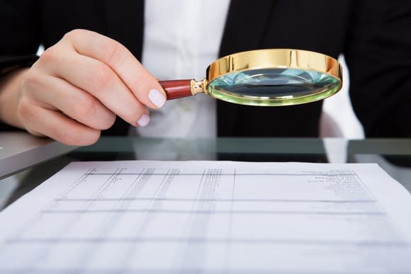 A woman holds a magnifying glass over a document.