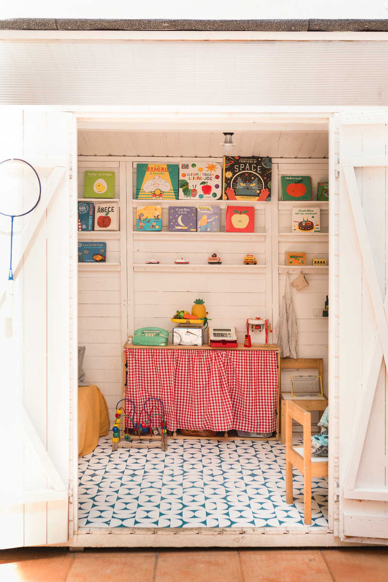 white kids' playroom with kitchen set, scale, cash register, table and chairs, and shelves with lots of books