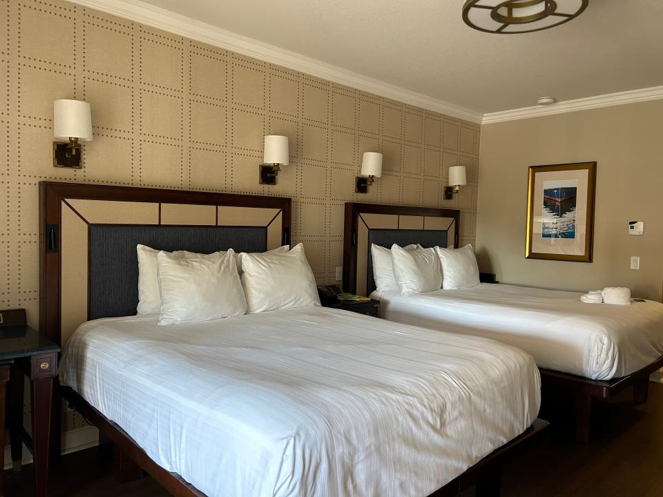 Two beds with white sheets in front of a simple beige wall in disney yacht club hotel room