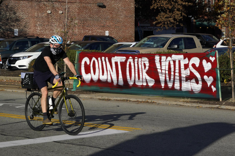 A bicyclist passes a Count Our Votes sign near the Allegheny County Election Division Warehouse on Pittsburgh's Northside where votes continue to be counted, Tuesday, Nov. 10, 2020. (AP Photo/Gene J. Puskar)