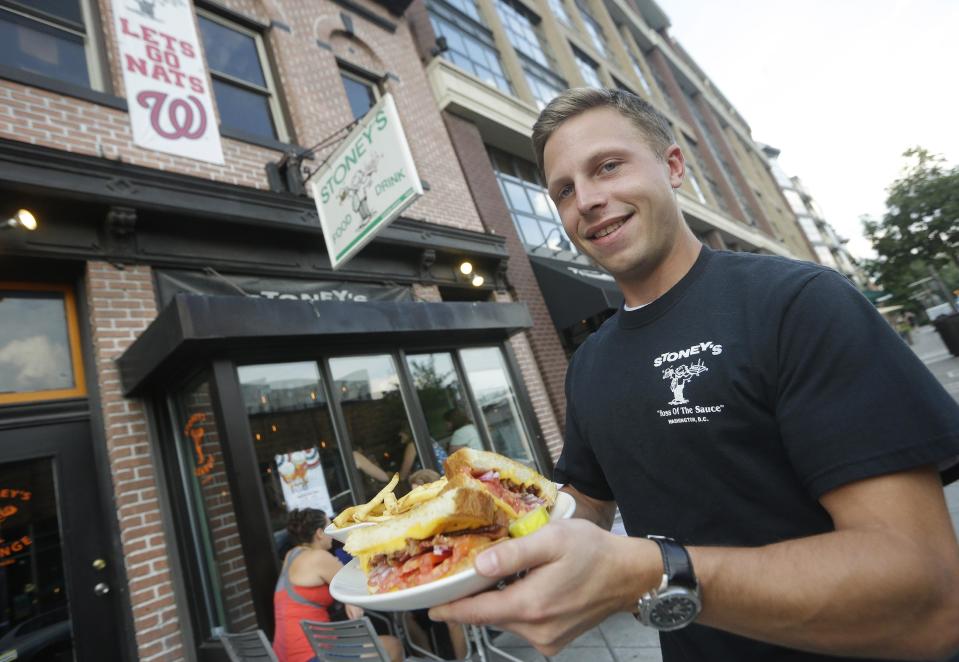 In this July 30, 2013 photo, manager Justin Glass holds a grilled cheese platter outside of Stoney's Lounge in Washington. Stoney's is located in the Logan Circle neighborhood of Washington. (AP Photo/Pablo Martinez Monsivais)