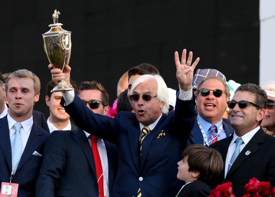 Trainer Bob Baffert hoists the trophy in the winner's circle after Victor Espinoza rode American Pharoah to win the Kentucky Derby at Churchill Downs. He's holding up four fingers to symbolize it marked his fourth Kentucky Derby victory.