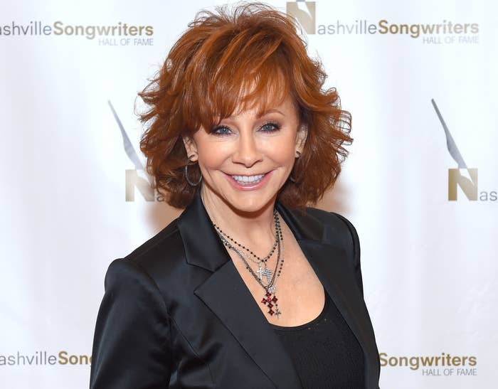 Reba wears a satin black blazer and cross necklaces