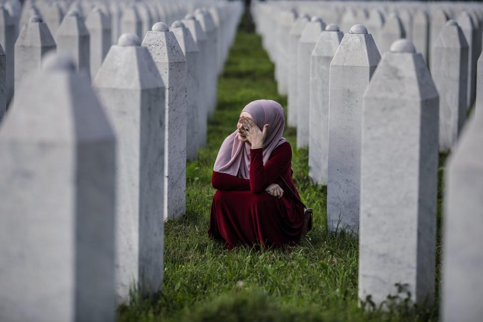 A woman in a head scarf cries surrounded by gravestones.