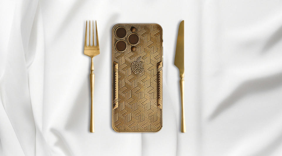 A gold-covered chocolate bar in the shape of the Apple iPhone 15 Pro Max with a gold knife and a fork