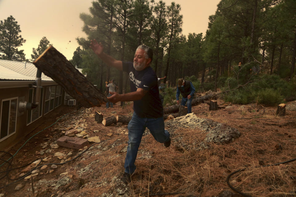 Chris Castillo throws a freshly-cut log as he and his cousins clear a wireline along a family member's home in Las Vegas, N.M., Monday, May 2, 2022. Wind-whipped flames are marching across more of New Mexico's tinder-dry mountainsides, forcing the evacuation of area residents and dozens of patients from the state's psychiatric hospital as firefighters scramble to keep new wildfires from growing. (AP Photo/Cedar Attanasio)