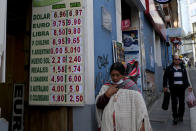 A woman walks by a sign showing the currency exchange rate in La Paz, Bolivia, Friday, June 28, 2024, two days after Army troops stormed the government palace in what President Luis Arce called a coup attempt. (AP Photo/Carlos Sanchez)