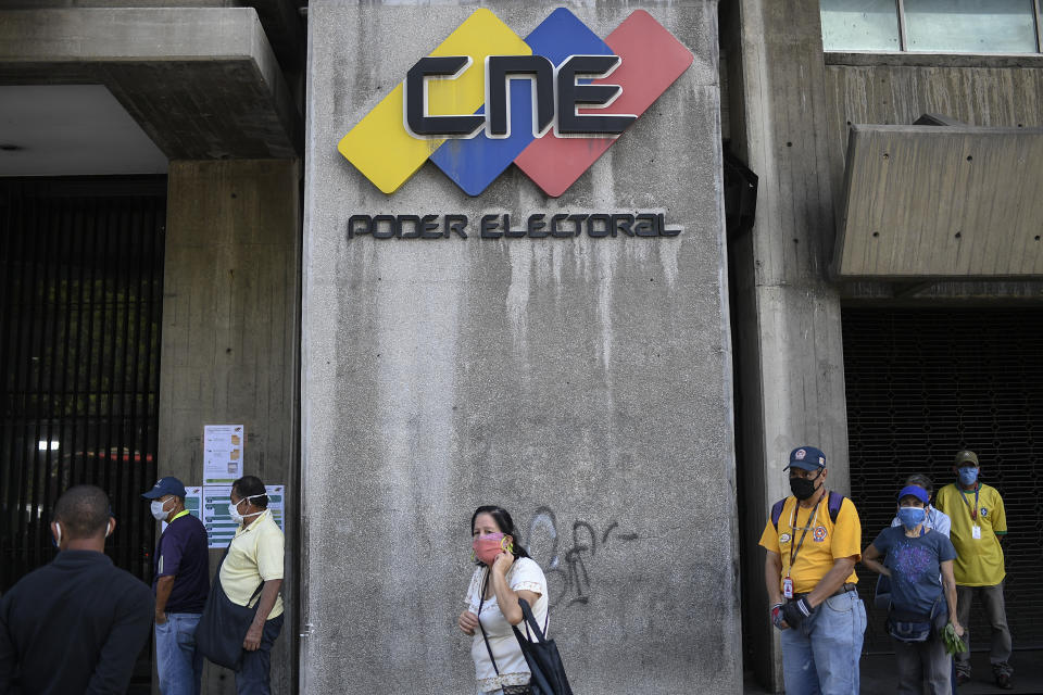 People, wearing protective face masks as a precaution against the spread of the new coronavirus, wait in a line near the entrance to an Electoral Council headquarters set up as a validation center to certify the authenticity of voter data in Caracas, Venezuela, Saturday, July 25, 2020. In a series of recent moves, the Supreme Court — loyal to President Nicolas Maduro — appointed a new elections commission, including three members who have been sanctioned by the U.S. and Canada, without the participation of the opposition-led congress, as the law requires. (AP Photo/Matias Delacroix)