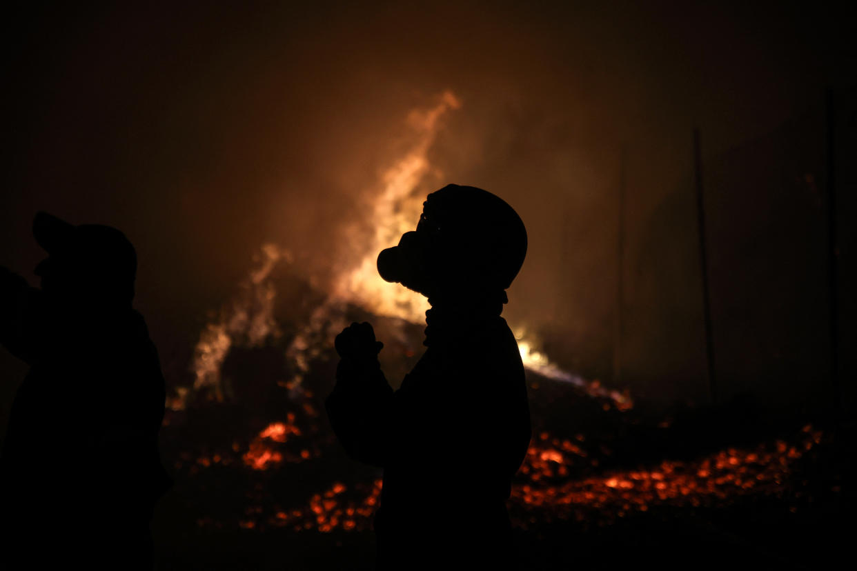 A firefighter wearing a breathing apparatus stands in front of flames in Vrilissia, Greece, on Monday.