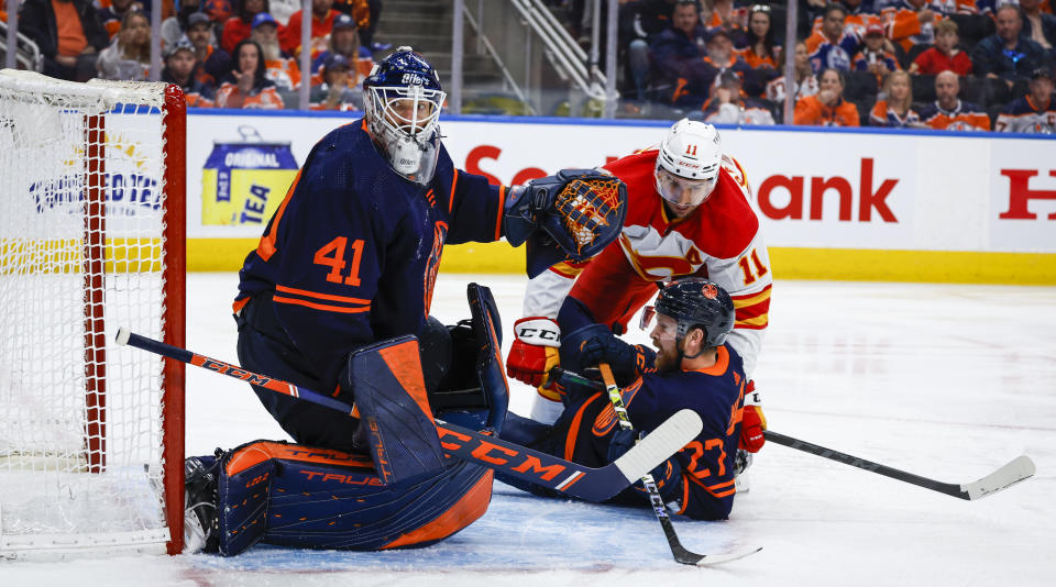 Calgary Flames forward Mikael Backlund, right, checks Edmonton Oilers defenceman Brett Kulak, center, in front of goalie Mike Smith during third period NHL second round playoff hockey action in Edmonton, Alberta, Sunday, May 22, 2022. (Jeff McIntosh/The Canadian Press via AP)