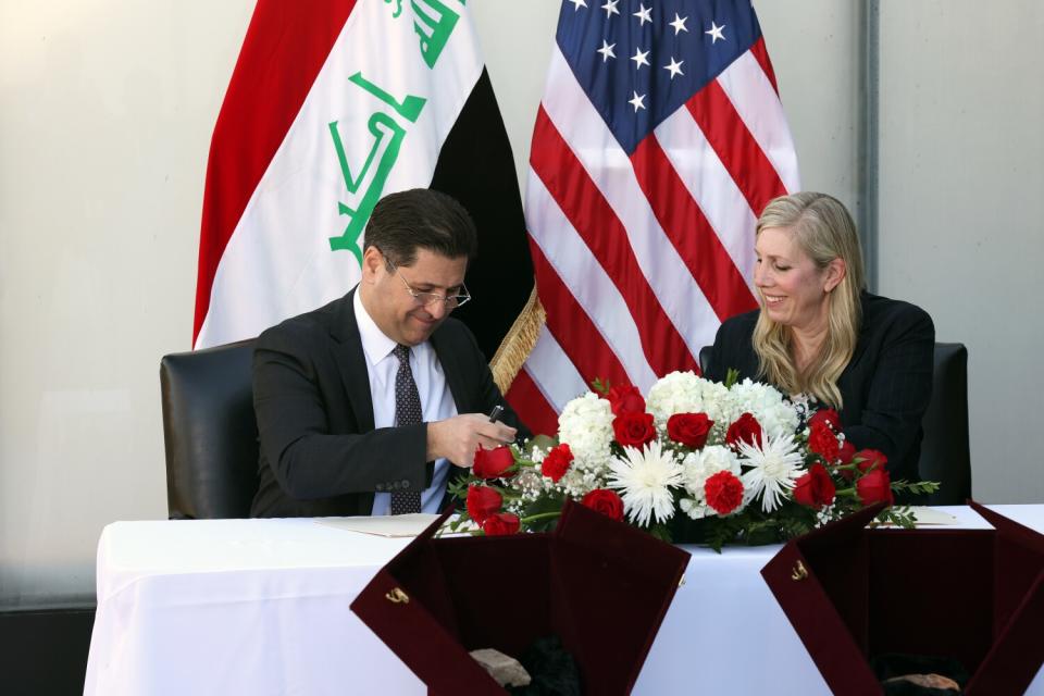 A ma and woman sit at a table with flowers on it and flags behind them