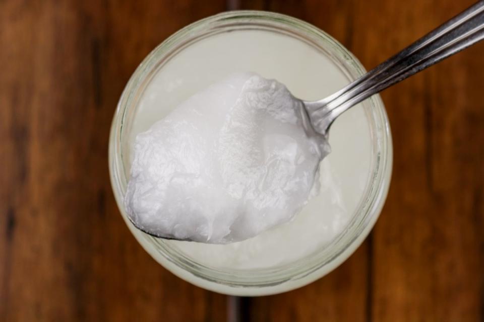 Spoonful of coconut oil from jar on wooden table.