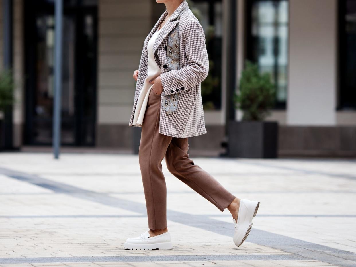woman walking down a street wearing a blazer, slacks, and loafers