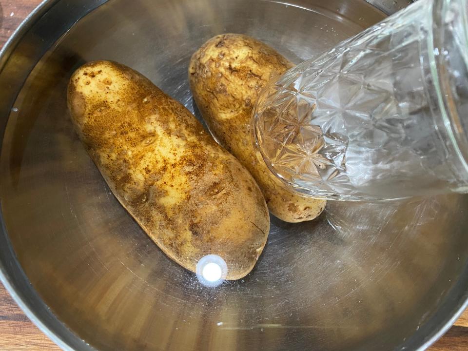 potatoes sitting in a bowl of water with a glass holding them down