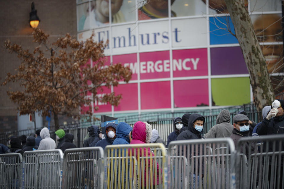 In this March 25, 2020 photo, patients wear personal protective equipment while maintaining social distancing as they wait in line for a COVID-19 test at Elmhurst Hospital Center in New York. (AP Photo/John Minchillo)