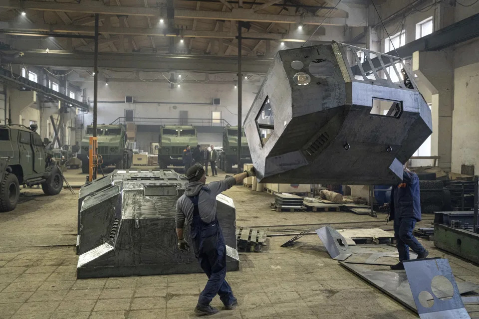 Workers moving by crane an armored artillery vehicle hood at a factory in Ukraine, on Wednesday, January 31, 2024. (AP Photo/Evgeniy Maloletka)