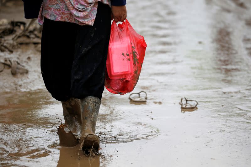 Woman carries a plastic bag containing food through the mud on a road after floods hit Bekasi