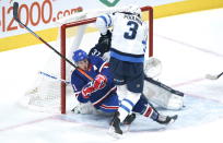 Montreal Canadiens' Brendan Gallagher is taken out from in front of Winnipeg Jets goaltender Connor Hellebuyck by defenseman Tucker Poolman during first-period NHL hockey game action in Montreal, Thursday, March 4, 2021. (Paul Chiasson/The Canadian Press via AP)