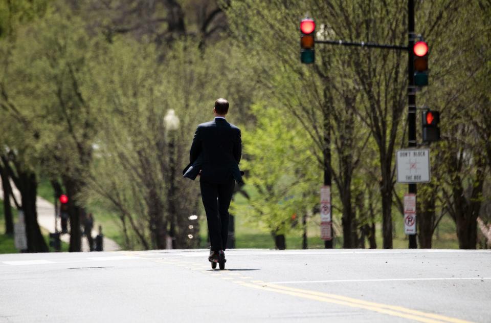 A man in a suit drives his electric scooter across a main street in Washington.