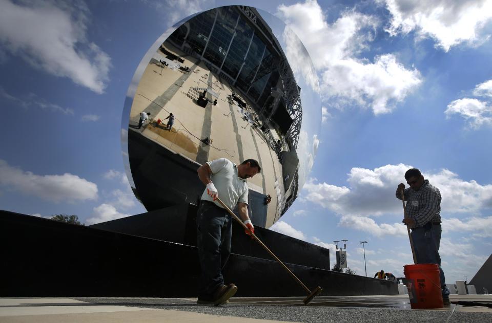 Anish Kapoor's "Sky Mirror", an art piece stands over Brent Hutchison, left, and Doroteo Camargo, right, as they two work on cleaning an area of the east end zone plaza outside AT&T Stadium, home of the Dallas Cowboys, Friday, Oct. 11, 2013, in Arlington, Texas. At 35 feet (11 meters) in diameter, the piece sits at an angle similar to a satellite dish. (AP Photo/Tony Gutierrez)