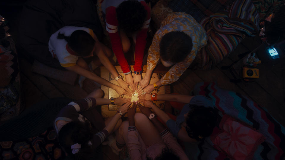 A group children hold hands in a circle around a board
