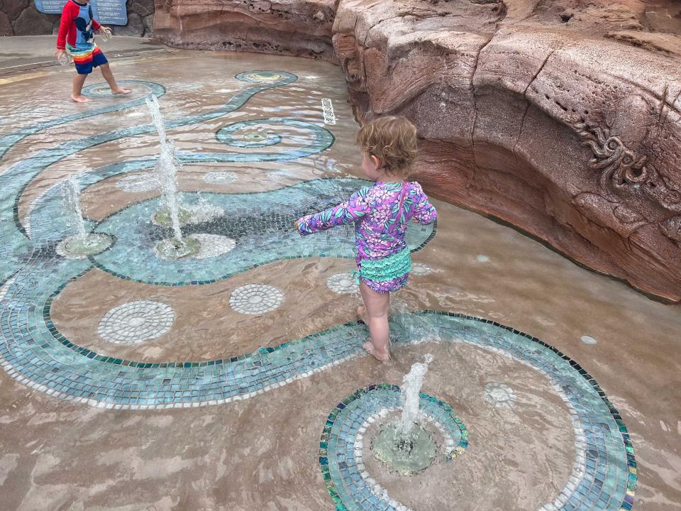 A toddler playing with fountains in a splash pad.