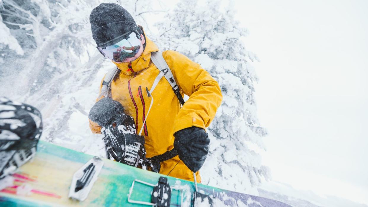 snowboarder in yellow jacket fixes his snowboard on a blustery day