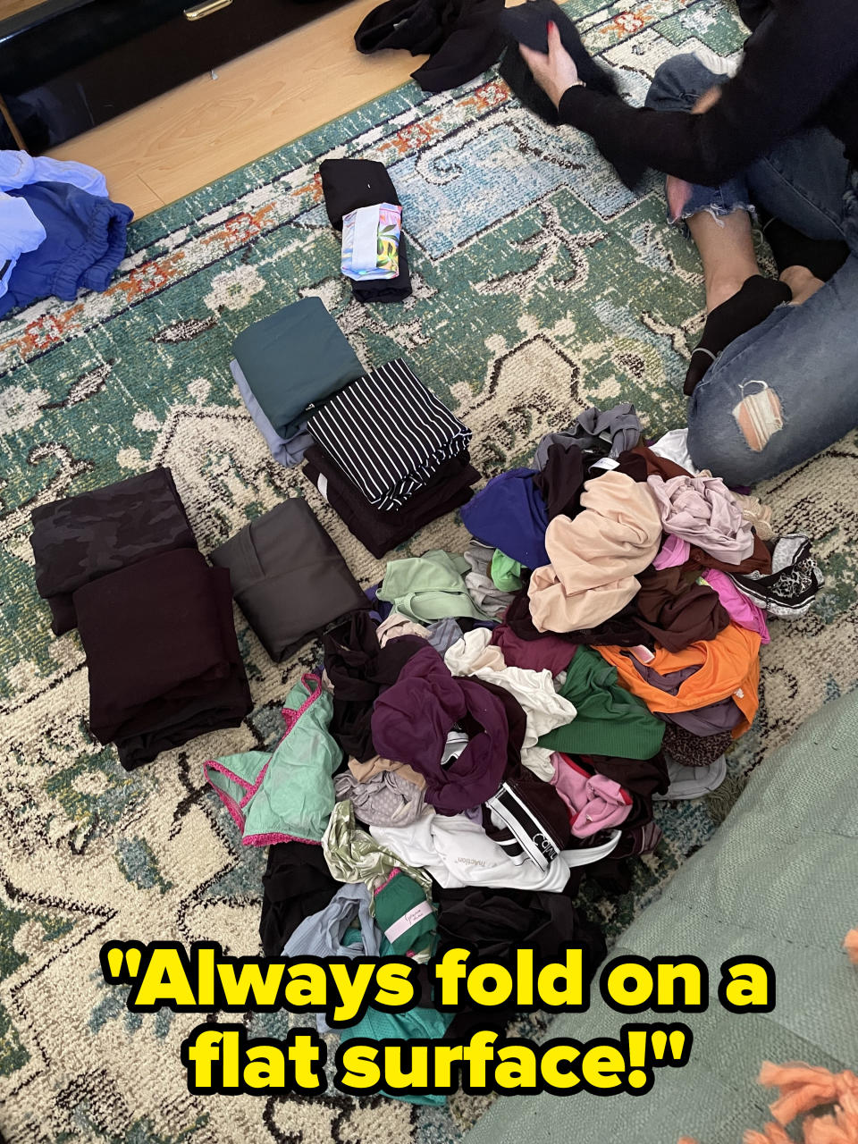 A pile of unfolded clothes pulled out of the drawers next to a small group of shirts that have been folded