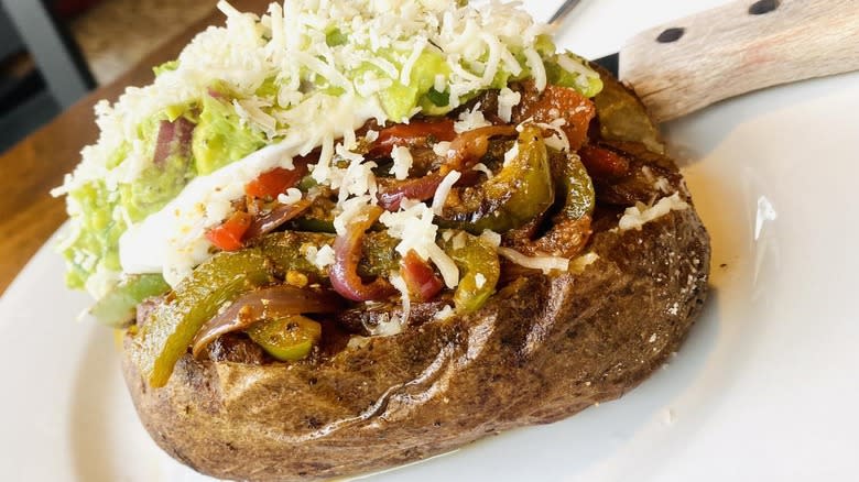 Baked potato with cooked peppers, guacamole, and shredded cheese