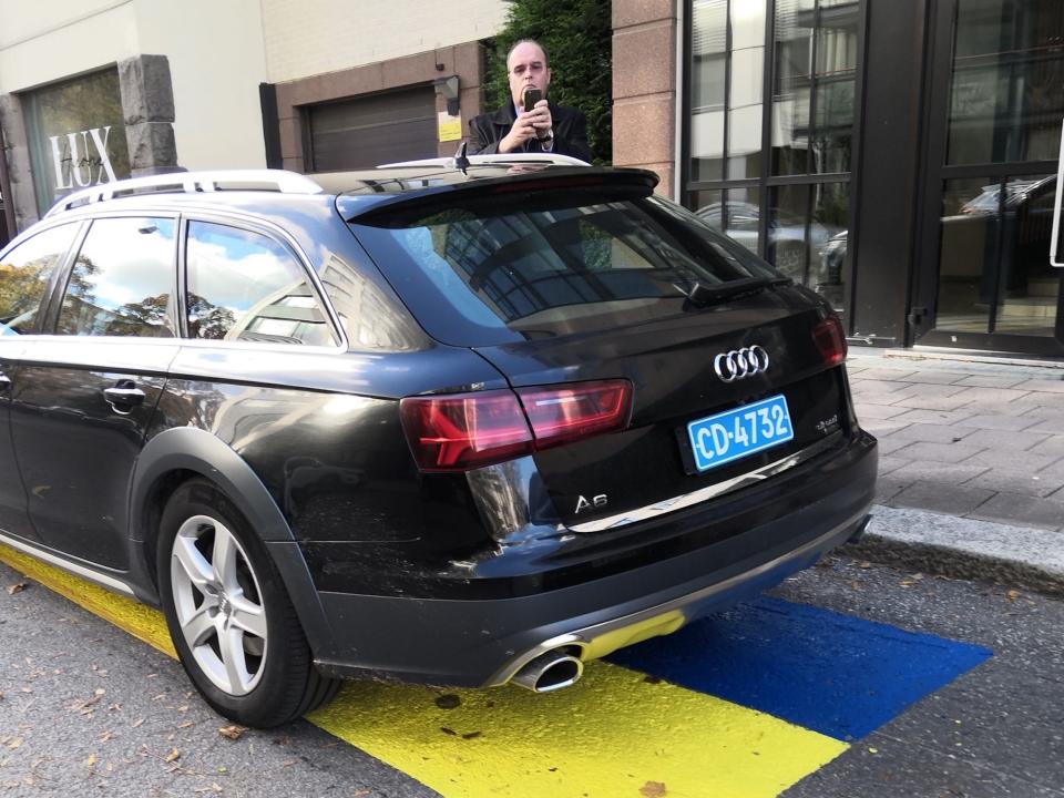 Russian Consul General to Finland Pyotr Plihin outside his official residence in Turku, Finland, on October 12, 2022. He stands behind his car parked on a spot painted with the Ukrainian flag. He looks angry and is taking a photo.