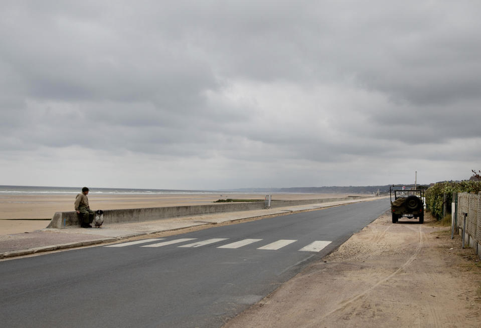 In this photo taken on Thursday, June 4, 2020, Eric Angely sits on a seawall in front of Omaha Beach, in WWII period dress near his parked WWII American Jeep, in Saint-Laurent-sur-Mer, Normandy, France. In sharp contrast to the 75th anniversary of D-Day, this year's 76th will be one of the loneliest remembrances ever, as the coronavirus pandemic is keeping nearly everyone from traveling. (AP Photo/Virginia Mayo)