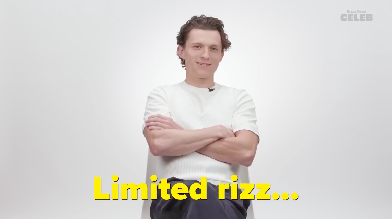 Tom Holland sits in a chair with arms folded, wearing a casual light shirt and dark pants. The text at the bottom reads, "Limited rizz..."