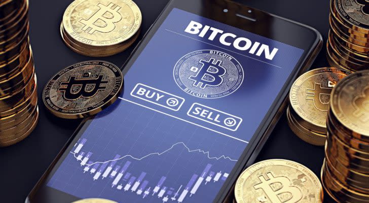 Smartphone with Bitcoin chart on-screen among piles of Bitcoins