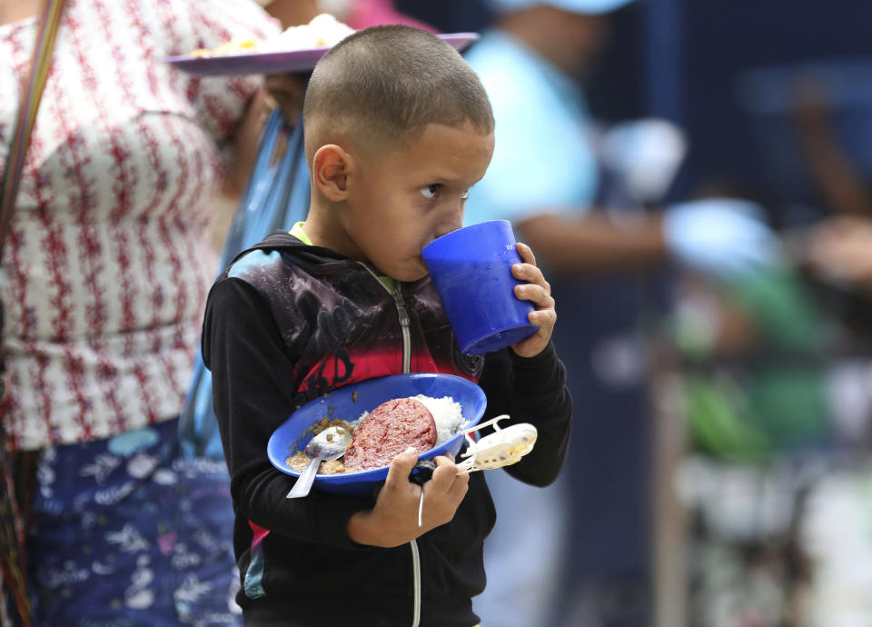 A boy takes a sip of a grape-flavored drink as he holds onto his free lunch at the "Divina Providencia" migrant shelter in La Parada, near Cucuta, Colombia, on the border with Venezuela, Monday, Feb. 18, 2019. The director of the shelter says they serve about 4,500 lunches per day, mostly to Venezuelan migrants, everyday of the week with the exception of Sunday. (AP Photo/Fernando Vergara)