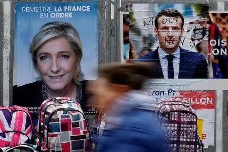 A woman walks past official posters of candidates for the 2017 French presidential election Marine Le Pen, French National Front (FN) political party leader (L) and Emmanuel Macron, head of the political movement En Marche !, or Onwards !, (R) at a local market in Bethune, France, April 24, 2017. REUTERS/Pascal Rossignol