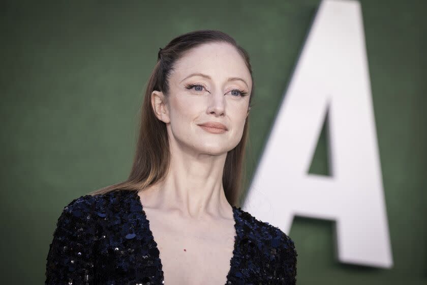 A woman in a sparkling dress poses in front of a large A