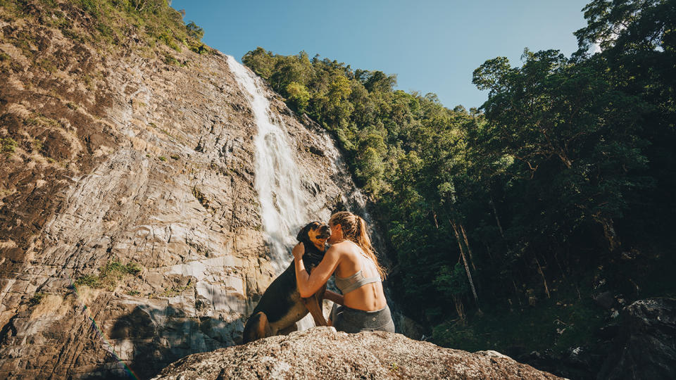 Dog sitting on rock with woman by waterfall