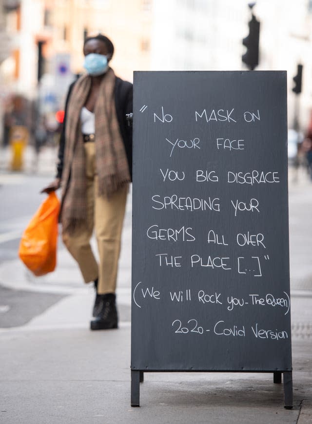 A person wearing a face mask walks past a sign encouraging the use of face coverings outside a cafe in central London