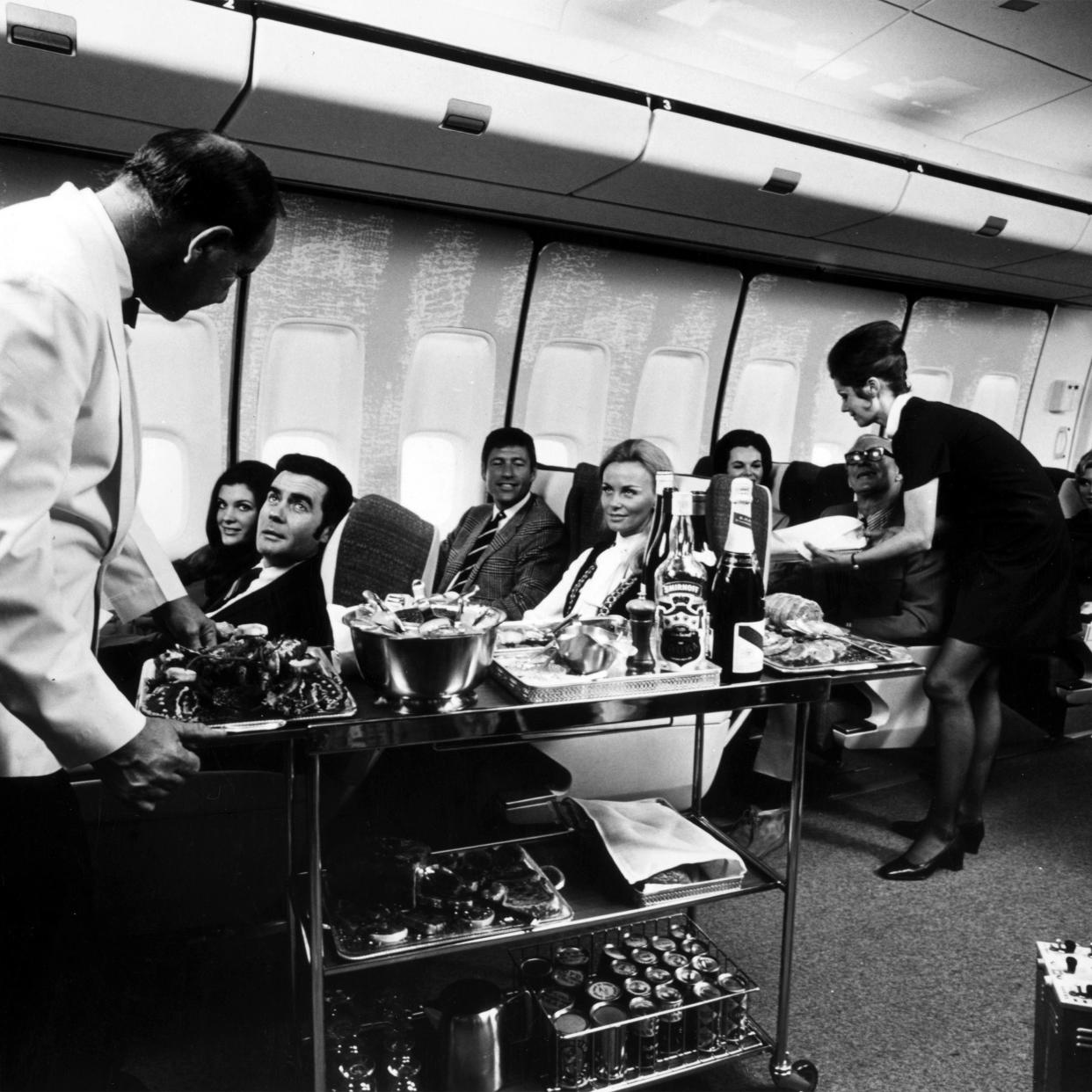 A steward and stewardess serving first-class passengers with drinks and refreshments on board a Boeing 747