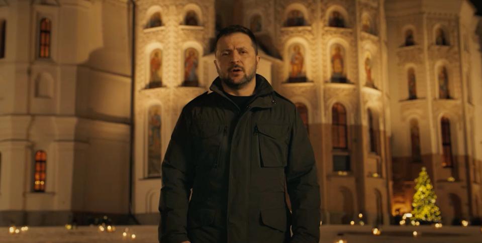Volodymy Zelenskyy in front of an ornate monastic building in Kyiv, Ukraine, with a Christmas tree in the background.