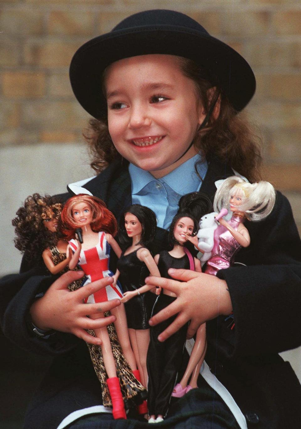 FILE - In this Thursday, October 16, 1997, file photo, Jodie Loftus, 4, holds an armload of the Spice Girls dolls when they were first unveiled at a fair of Christmas toys in London. From left to right the dolls are Scary Spice, Ginger Spice, Posh Spice, Sporty Spice and Baby Spice. Spice Girl dolls were one of the hottest toys during the 1999 holiday season. (AP Photo/Lynne Sladky)