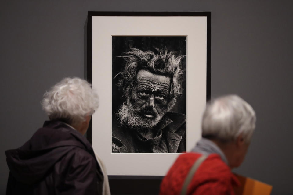 Visitors look at and walk past a 1970 photograph of a homeless Irishman in the Spitalfields area of east London by veteran British conflict photographer Don McCullin at the launch of his retrospective exhibition at the Tate Britain gallery in London, Monday, Feb. 4, 2019. The exhibition includes over 250 of his black and white photographs, including conflict images from the Vietnam war, Northern Ireland, Cyprus, Lebanon and Biafra, alongside landscape and still life images. (AP Photo/Matt Dunham)