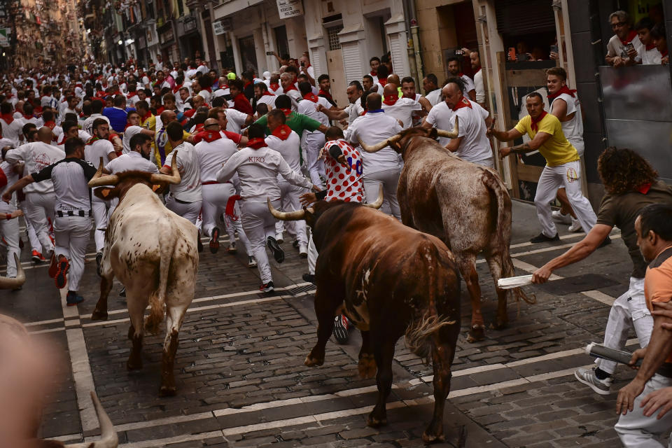 Decenas de personas corren delante de los toros por las calles del centro de Pamplona, en el norte de España, en el último día de los encierros de San Fermín, el 14 de julio de 2022. (AP Foto/Álvaro Barrientos)