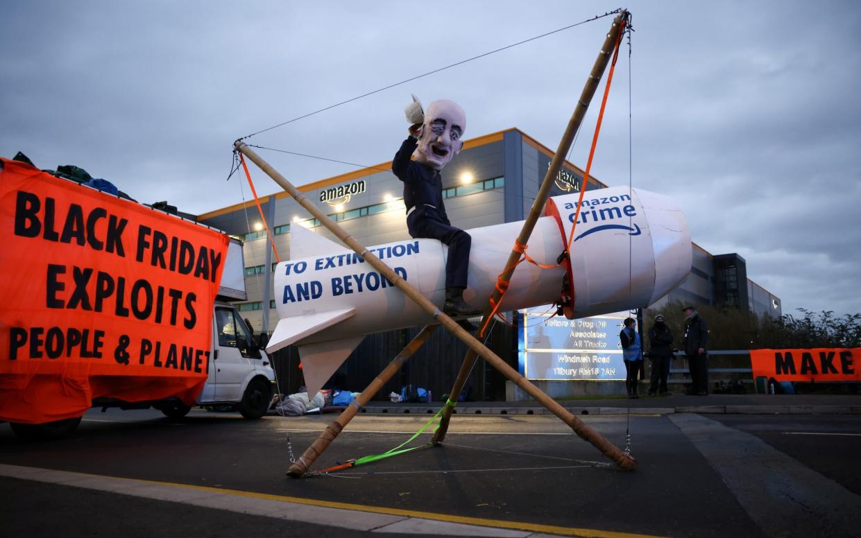 A person wearing a head mask depicting Amazon founder Jeff Bezos sits on a fake rocket as Extinction Rebellion activists block an entrance to an Amazon fulfilment centre in Tilbury, Essex, Britain, November 26, 2021. - Henry Nicholls/Reuters