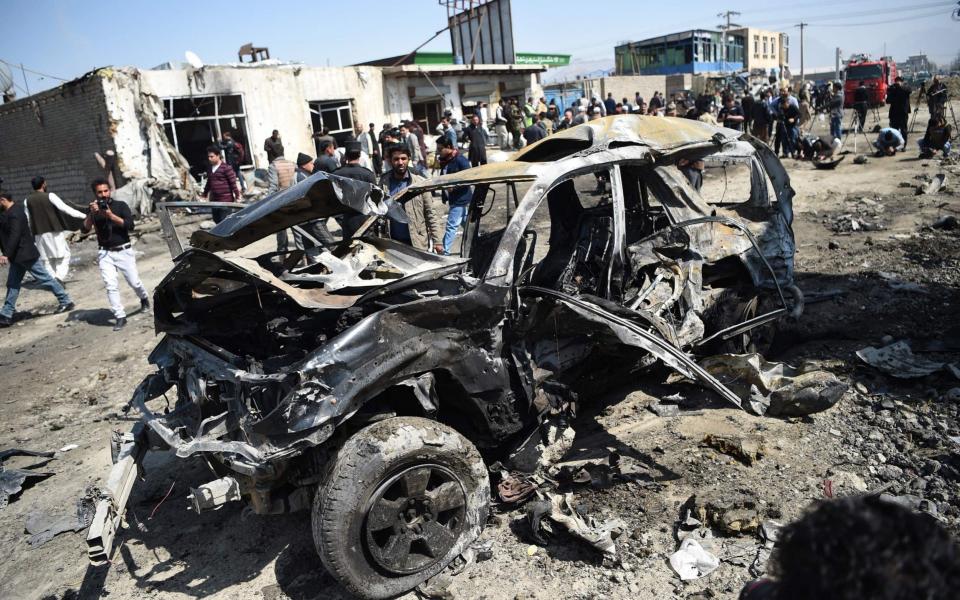 Afghan security personnel and civilians gather next to a damaged car at the site of a car bomb attack in Kabul  - AFP
