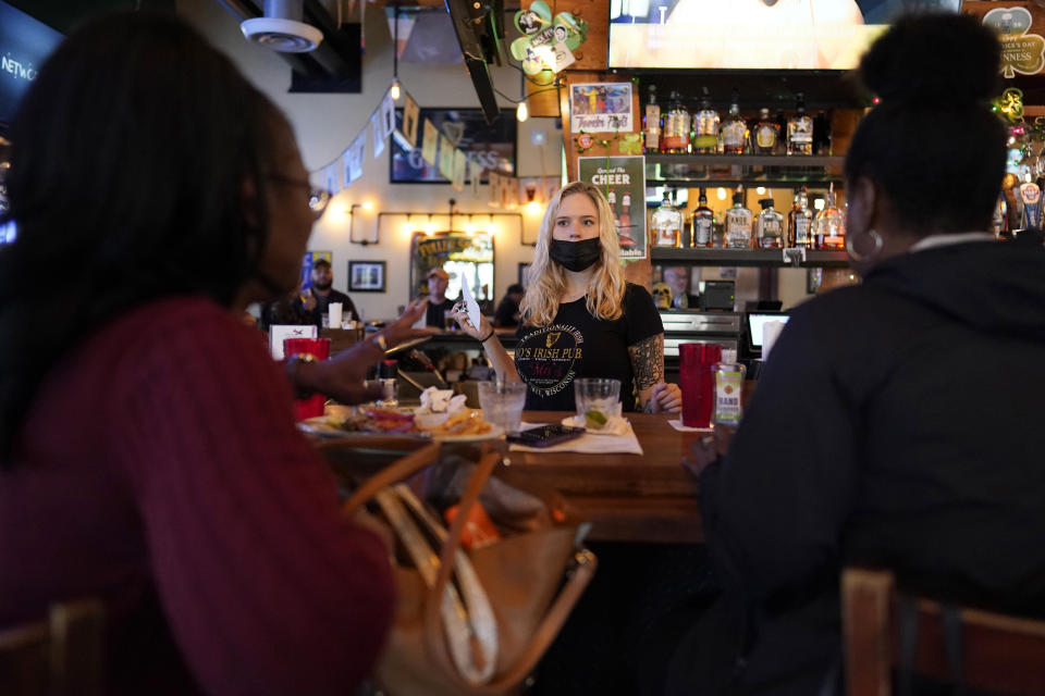 FILE - In this March 10, 2021, file photo, bartender Angie Gibson, center, waits on Monica Ponton, left, and Devona Williams, right, at Mo's Irish Pub in Houston. Optimism is spreading in the U.S. as COVID-19 deaths plummet and states ease restrictions and open vaccinations to younger adults. But across Europe, dread is setting in with another wave of infections that is closing schools and cafes and bringing new lockdowns. (AP Photo/David J. Phillip, File)