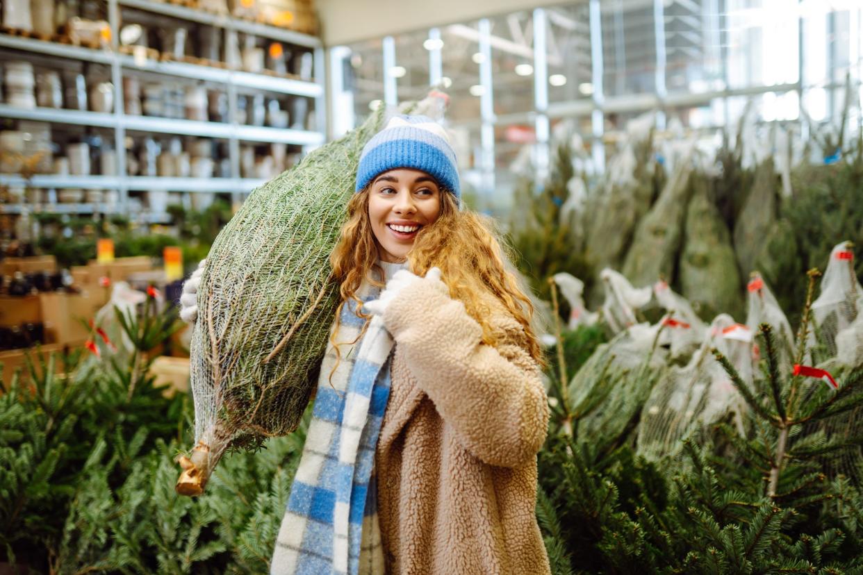 Beautiful young woman buys a Christmas tree at the fair. She chooses a beautiful Christmas tree for her home interior. New Year's holiday concept